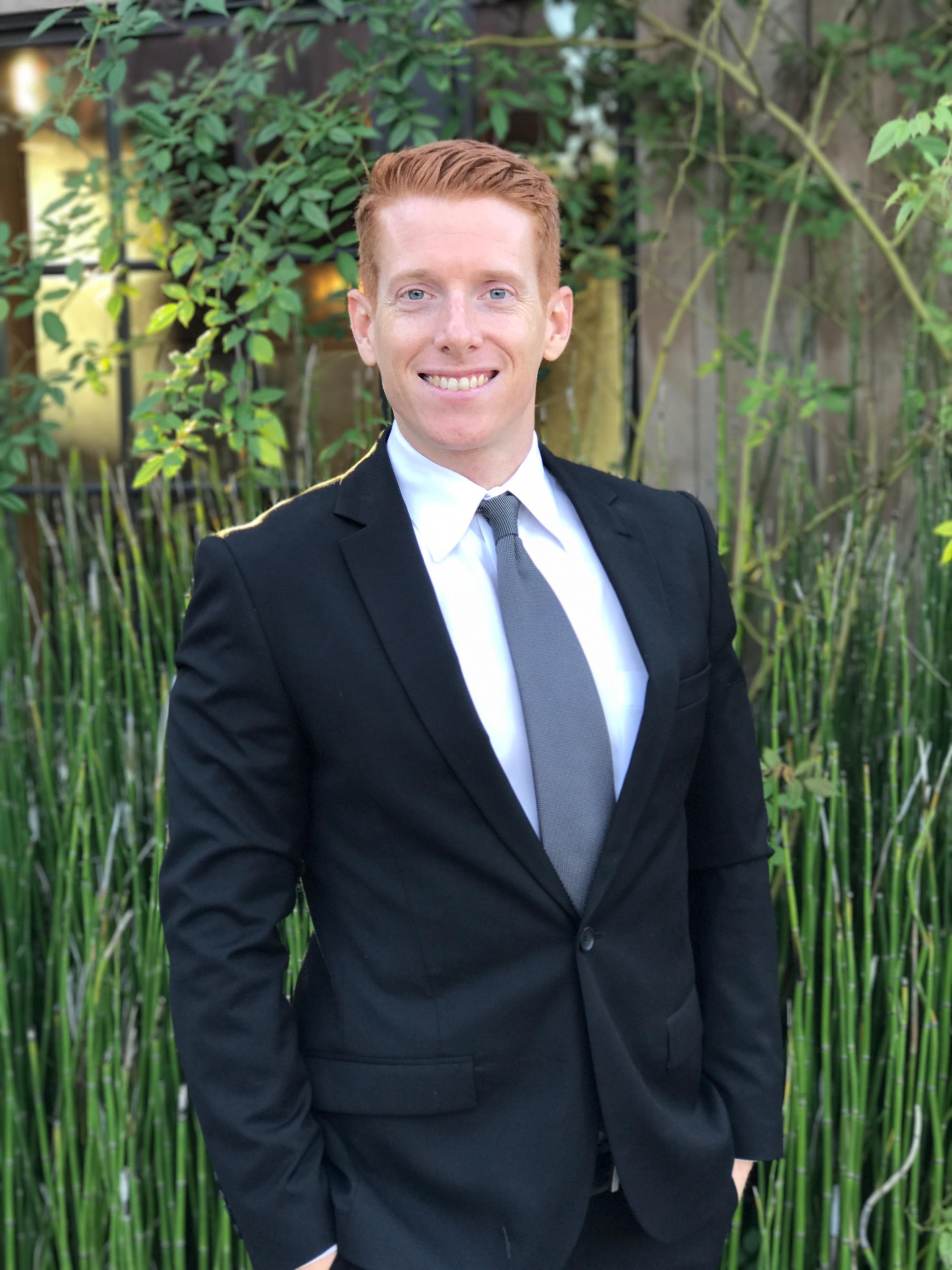 Kevin in suit and tie smiling in front of plants